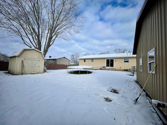 yard layered in snow featuring a trampoline and a storage unit