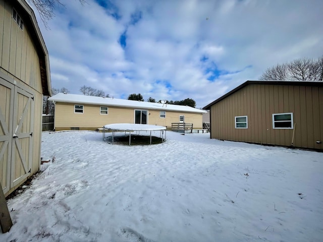 snow covered house featuring a storage shed and a trampoline