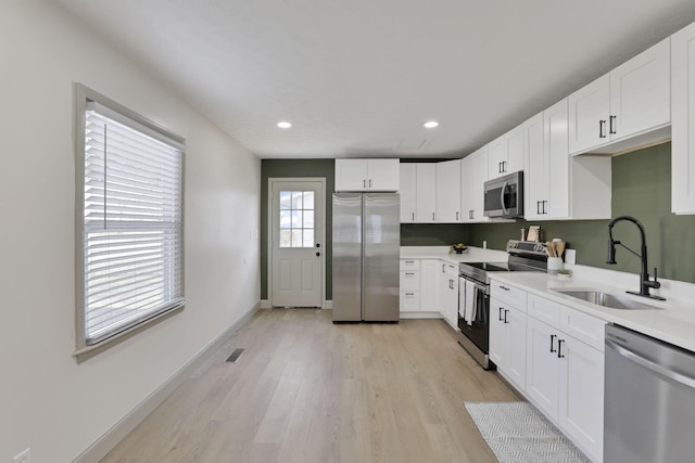 kitchen with white cabinets, light hardwood / wood-style floors, sink, and appliances with stainless steel finishes