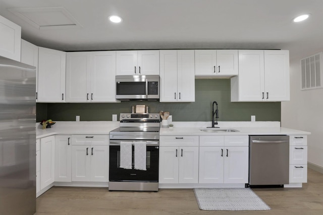 kitchen with sink, white cabinets, light wood-type flooring, and appliances with stainless steel finishes