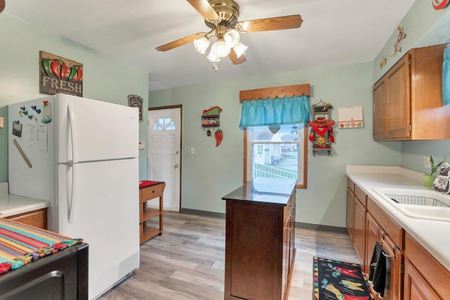 kitchen with light wood-type flooring, white fridge, ceiling fan, and sink