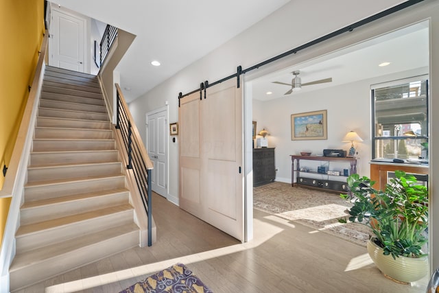 stairs featuring hardwood / wood-style floors, a barn door, and ceiling fan