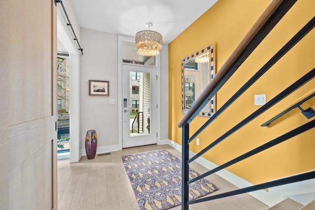 entrance foyer with a chandelier, light wood-type flooring, and a barn door