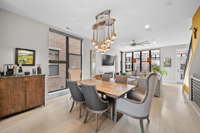 dining space with ceiling fan with notable chandelier and light wood-type flooring