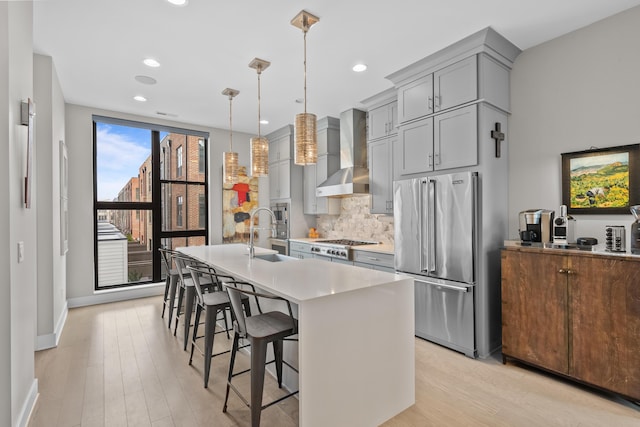 kitchen featuring pendant lighting, a breakfast bar, backsplash, wall chimney exhaust hood, and appliances with stainless steel finishes