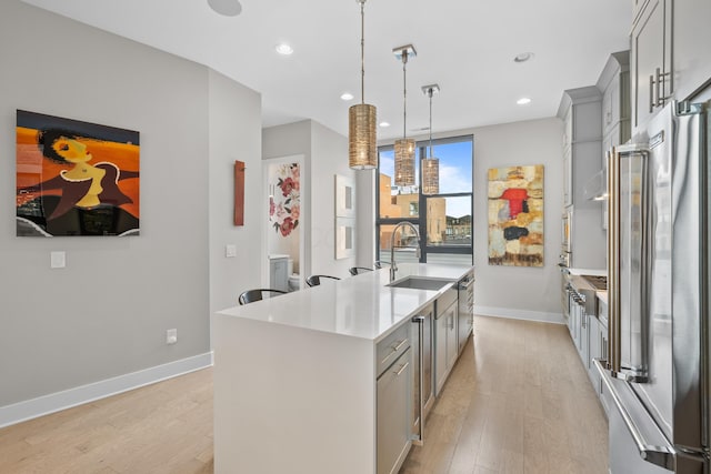 kitchen with high quality fridge, gray cabinetry, sink, a center island with sink, and hanging light fixtures