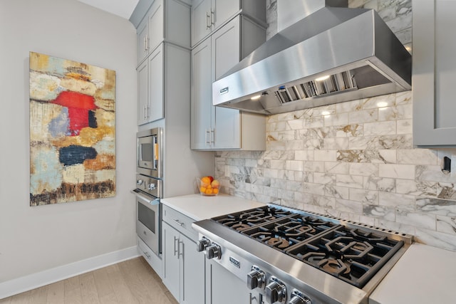 kitchen with light wood-type flooring, tasteful backsplash, wall chimney exhaust hood, stainless steel appliances, and gray cabinets