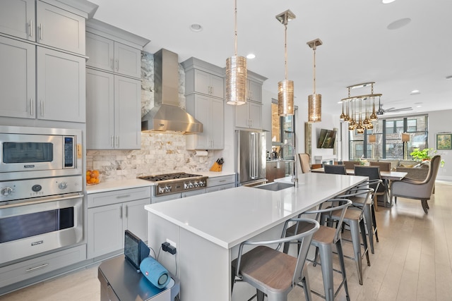 kitchen featuring tasteful backsplash, wall chimney exhaust hood, stainless steel appliances, sink, and hanging light fixtures