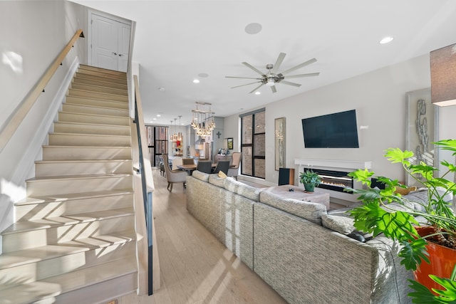 living room featuring ceiling fan with notable chandelier and light wood-type flooring