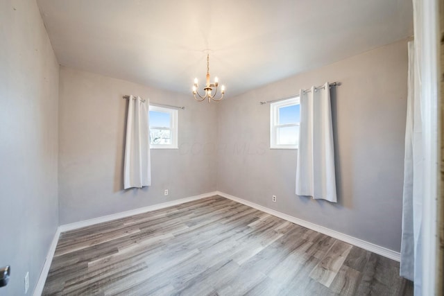 unfurnished room with plenty of natural light, a chandelier, and light wood-type flooring