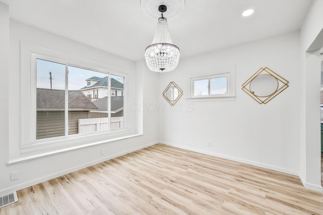 unfurnished dining area featuring a healthy amount of sunlight, a notable chandelier, and light wood-type flooring