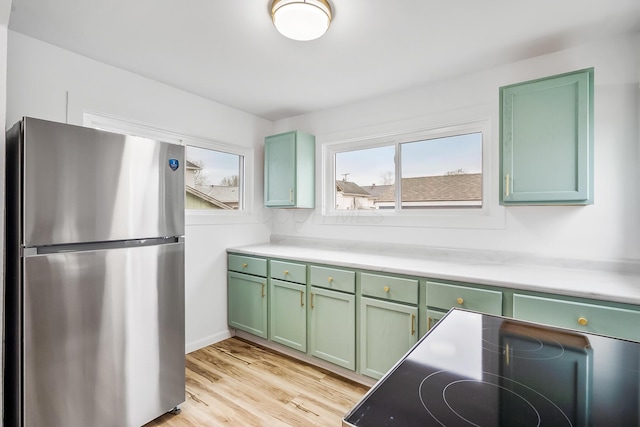 kitchen featuring green cabinetry, stove, stainless steel refrigerator, and light hardwood / wood-style floors