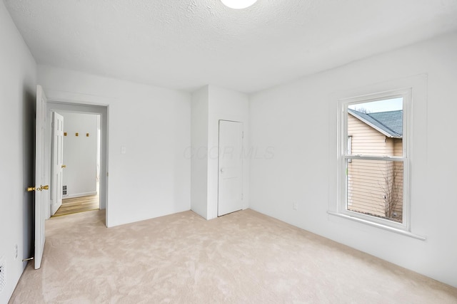 unfurnished bedroom featuring multiple windows, light carpet, and a textured ceiling