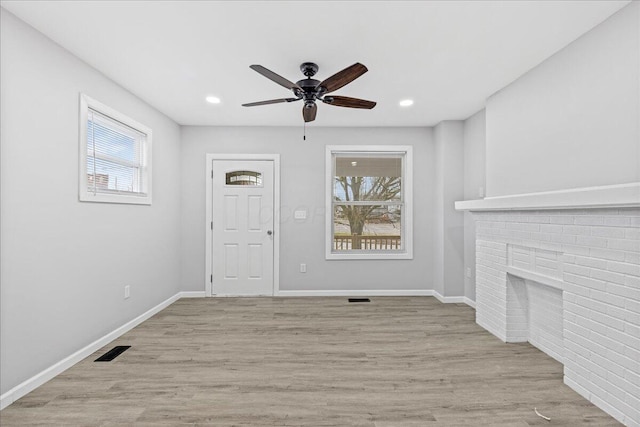 unfurnished living room with a brick fireplace, ceiling fan, a healthy amount of sunlight, and light wood-type flooring