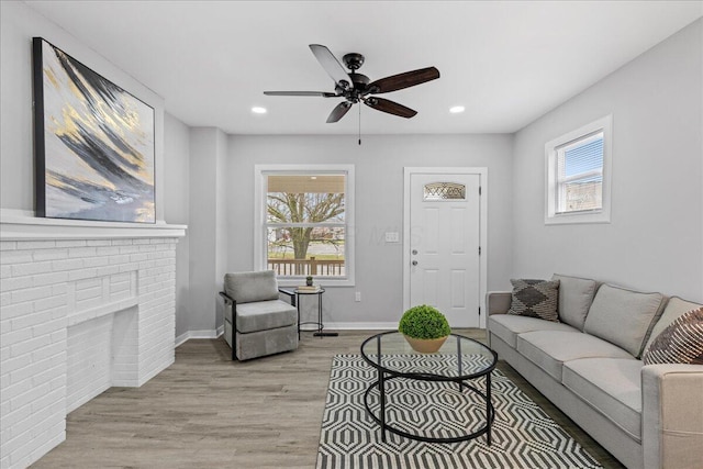 living room featuring a fireplace, ceiling fan, light hardwood / wood-style flooring, and a healthy amount of sunlight