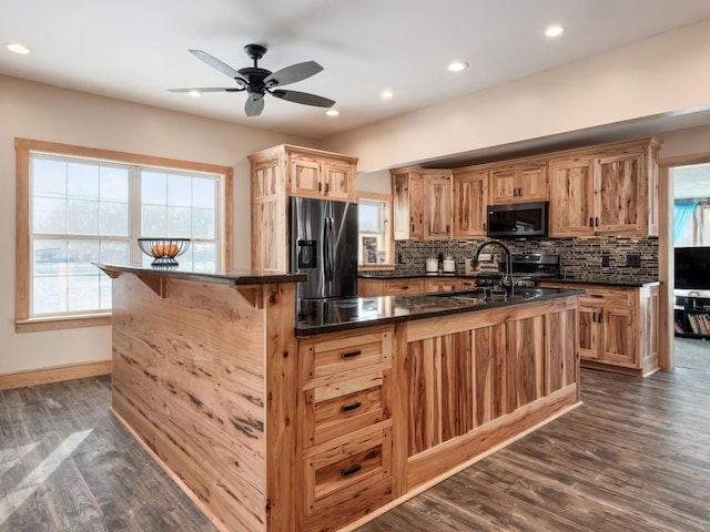 kitchen with stainless steel refrigerator with ice dispenser, dark wood-type flooring, a healthy amount of sunlight, and an island with sink