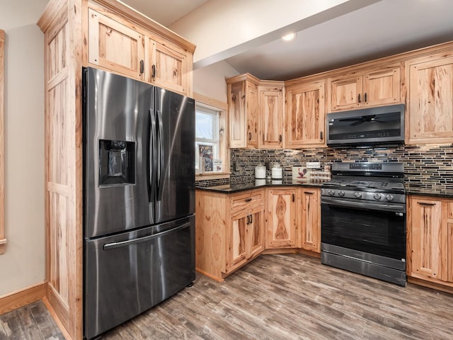 kitchen with hardwood / wood-style flooring, appliances with stainless steel finishes, dark stone countertops, and tasteful backsplash