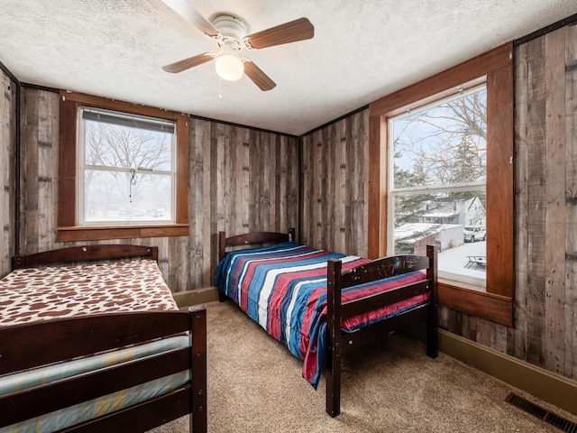 bedroom featuring ceiling fan, multiple windows, wood walls, and light carpet