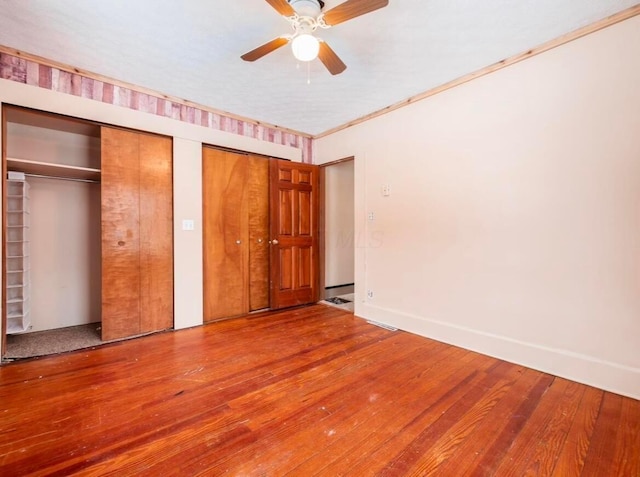 unfurnished bedroom featuring crown molding, wood-type flooring, two closets, and ceiling fan