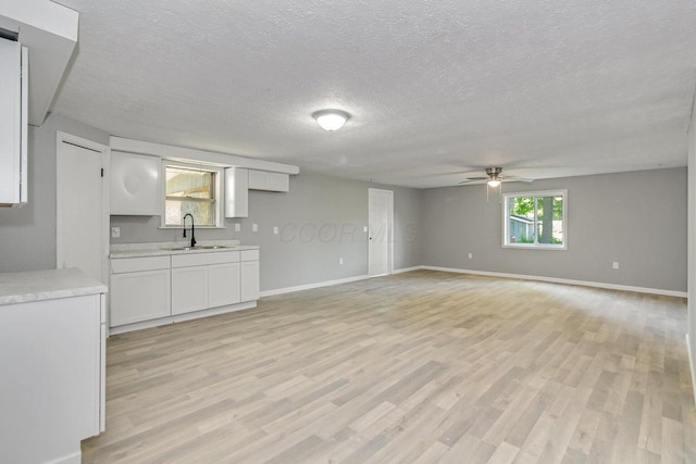 unfurnished living room featuring ceiling fan, sink, a textured ceiling, and light hardwood / wood-style flooring