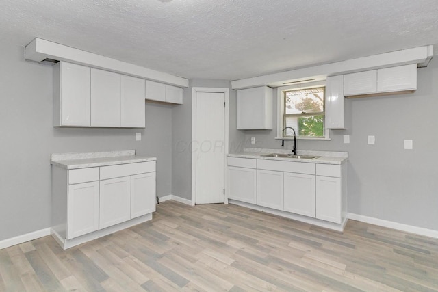 kitchen featuring light wood-type flooring, a textured ceiling, white cabinetry, and sink