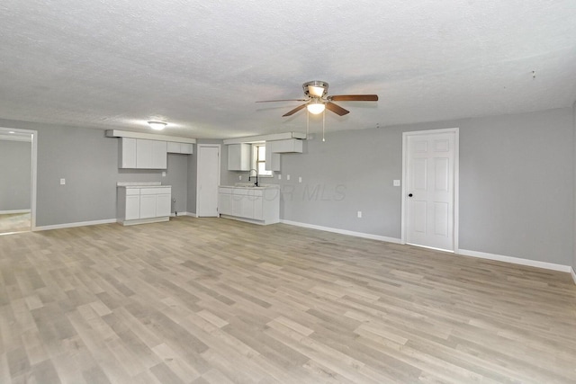 unfurnished living room featuring a textured ceiling, light hardwood / wood-style flooring, ceiling fan, and sink