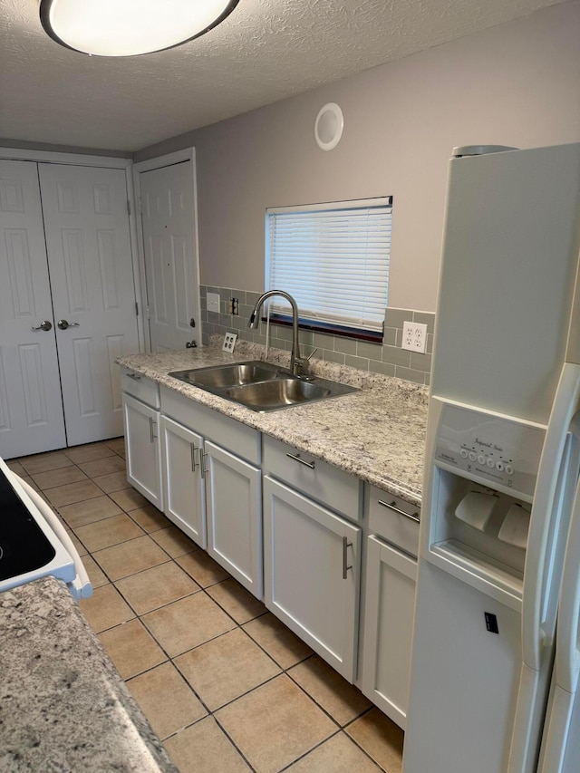 kitchen featuring backsplash, sink, white refrigerator with ice dispenser, white cabinets, and light tile patterned flooring
