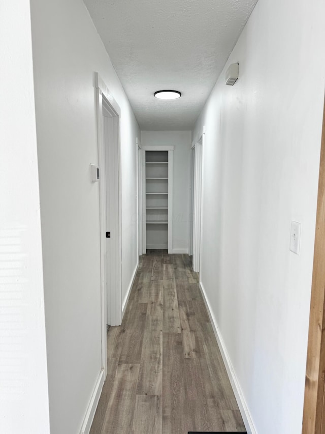 corridor featuring a textured ceiling, baseboards, and wood finished floors