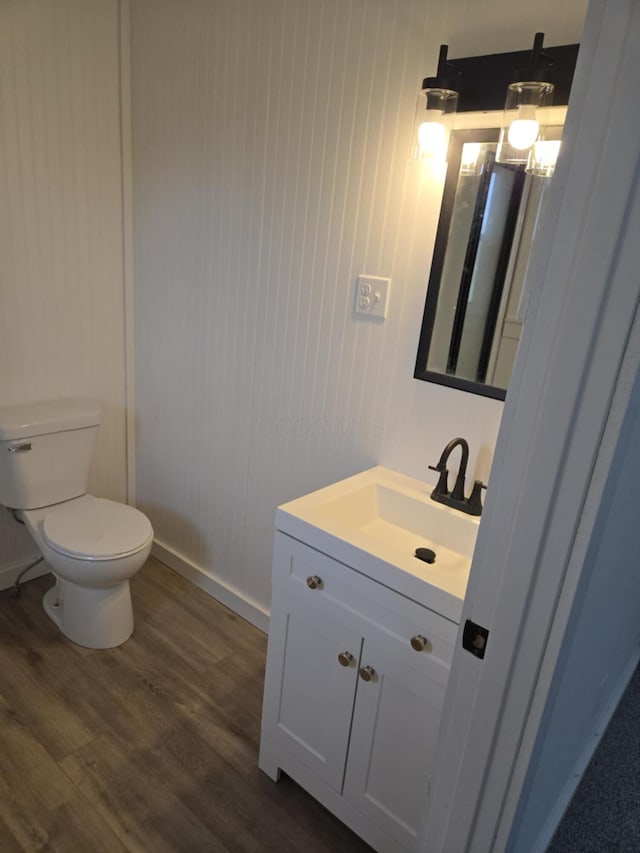 half bathroom with toilet, vanity, baseboards, and wood finished floors