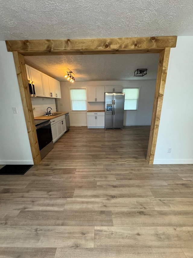 kitchen featuring light wood-style flooring, stainless steel appliances, a textured ceiling, white cabinetry, and a sink