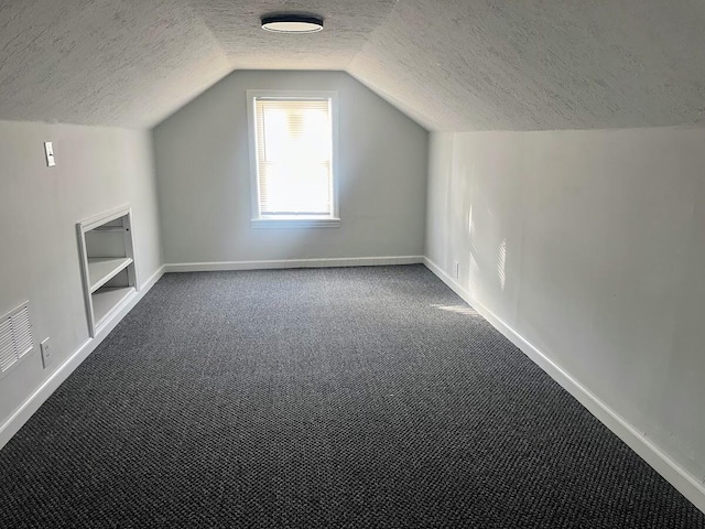 additional living space featuring built in shelves, lofted ceiling, carpet, and a textured ceiling