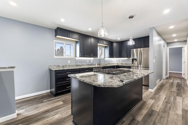 kitchen with hanging light fixtures, light stone counters, dark hardwood / wood-style floors, a kitchen island, and appliances with stainless steel finishes