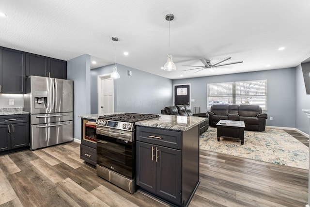 kitchen featuring appliances with stainless steel finishes, light stone counters, dark wood-type flooring, decorative light fixtures, and a center island