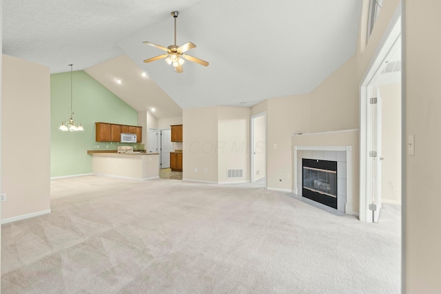 unfurnished living room with a tile fireplace, ceiling fan with notable chandelier, light carpet, and high vaulted ceiling