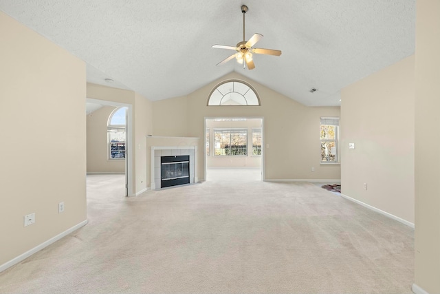 unfurnished living room with a tiled fireplace, vaulted ceiling, a textured ceiling, and a wealth of natural light