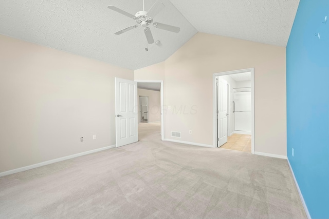 unfurnished bedroom featuring lofted ceiling, ensuite bath, ceiling fan, a textured ceiling, and light carpet