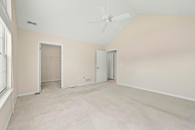 unfurnished bedroom with a spacious closet, light colored carpet, high vaulted ceiling, a closet, and ceiling fan