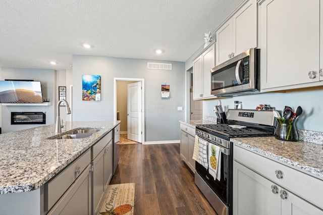 kitchen with sink, dark hardwood / wood-style floors, a textured ceiling, a center island with sink, and appliances with stainless steel finishes