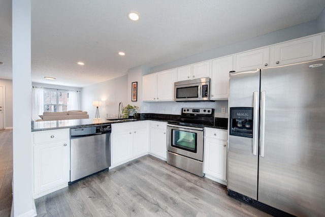 kitchen with sink, kitchen peninsula, appliances with stainless steel finishes, white cabinets, and light wood-type flooring