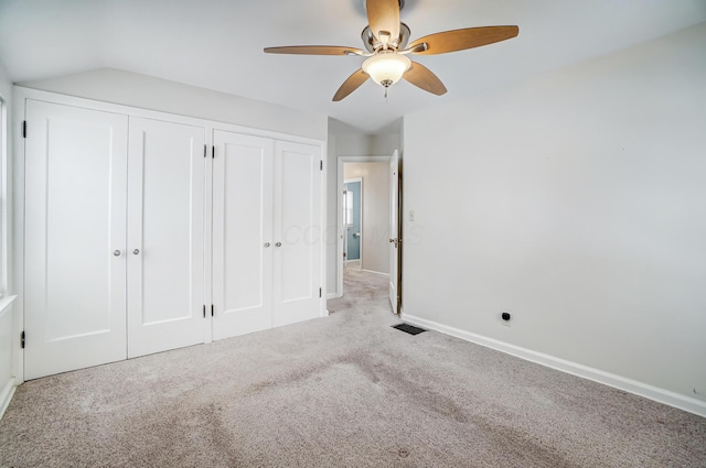 unfurnished bedroom with ceiling fan, vaulted ceiling, light carpet, and two closets