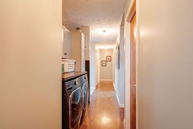 clothes washing area with cabinets, washer and clothes dryer, a textured ceiling, and light hardwood / wood-style floors