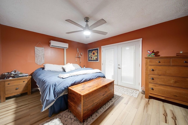 bedroom with a wall unit AC, ceiling fan, a textured ceiling, and light wood-type flooring