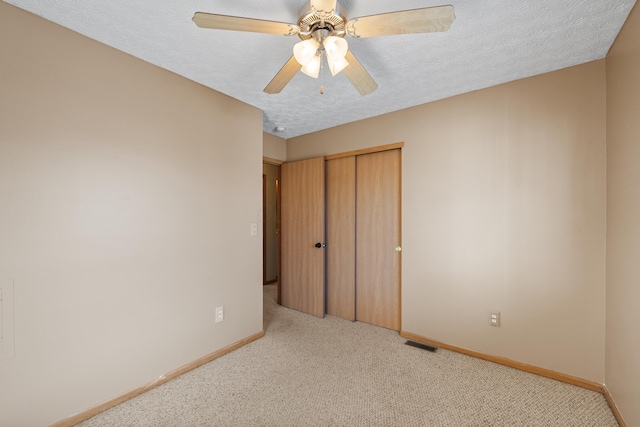 unfurnished bedroom featuring ceiling fan, light colored carpet, a textured ceiling, and a closet