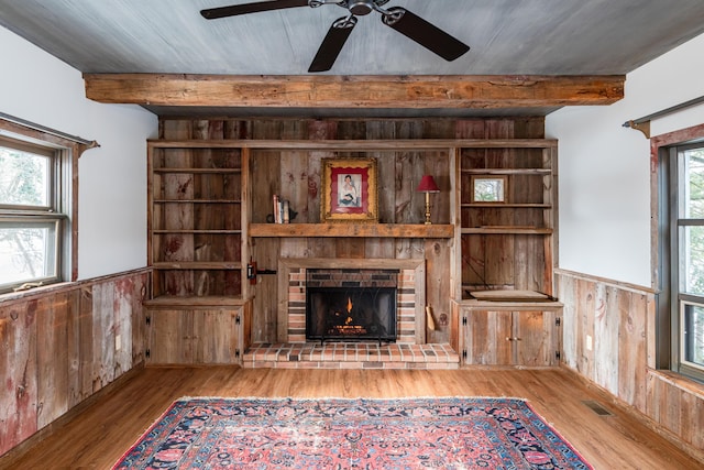 unfurnished living room featuring beamed ceiling, a brick fireplace, wooden walls, and light hardwood / wood-style flooring