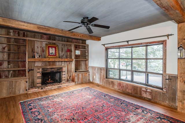 unfurnished living room with hardwood / wood-style flooring, a fireplace, wooden walls, and ceiling fan