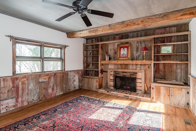 living room with beamed ceiling, a fireplace, light hardwood / wood-style floors, and wood walls