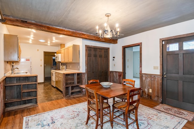 dining space with sink, wooden walls, dark hardwood / wood-style floors, a notable chandelier, and beam ceiling