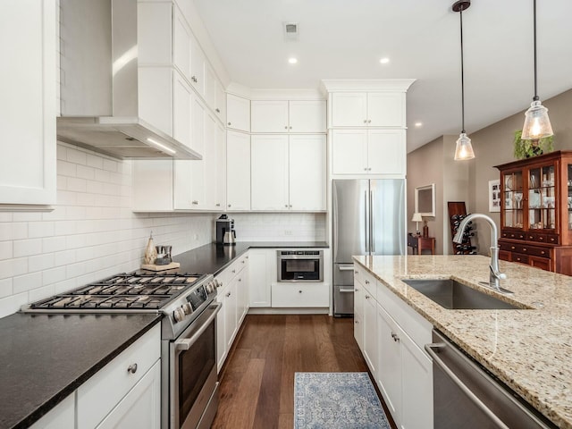 kitchen with appliances with stainless steel finishes, decorative backsplash, pendant lighting, wall chimney exhaust hood, and sink