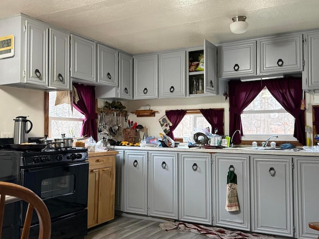 kitchen with a textured ceiling, gray cabinetry, hardwood / wood-style floors, and black gas range oven