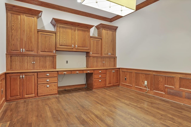 unfurnished office featuring built in desk, hardwood / wood-style flooring, and ornamental molding